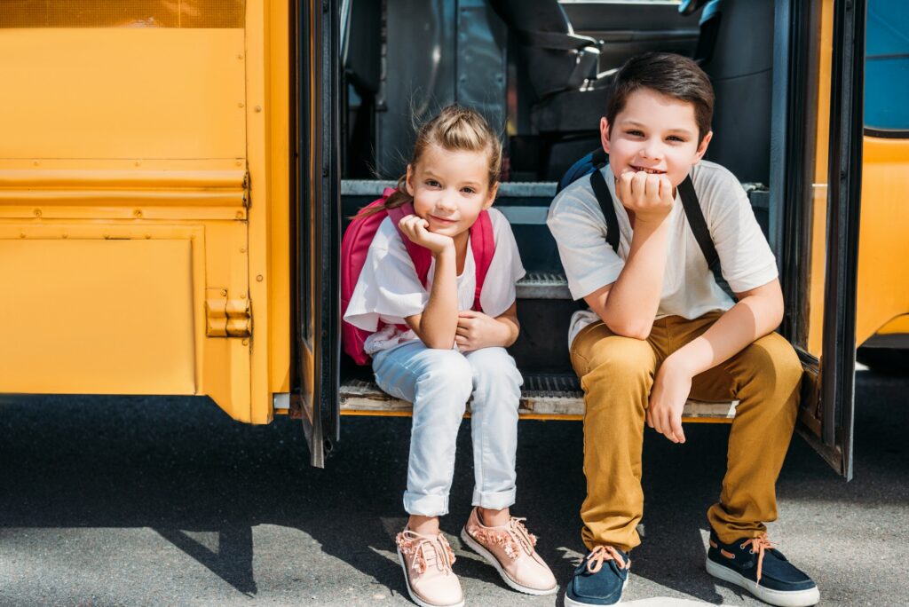 adorable little scholars sitting on stairs of school bus